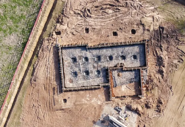 Vista aérea de obra com blocos de fundação executados em solo vermelho